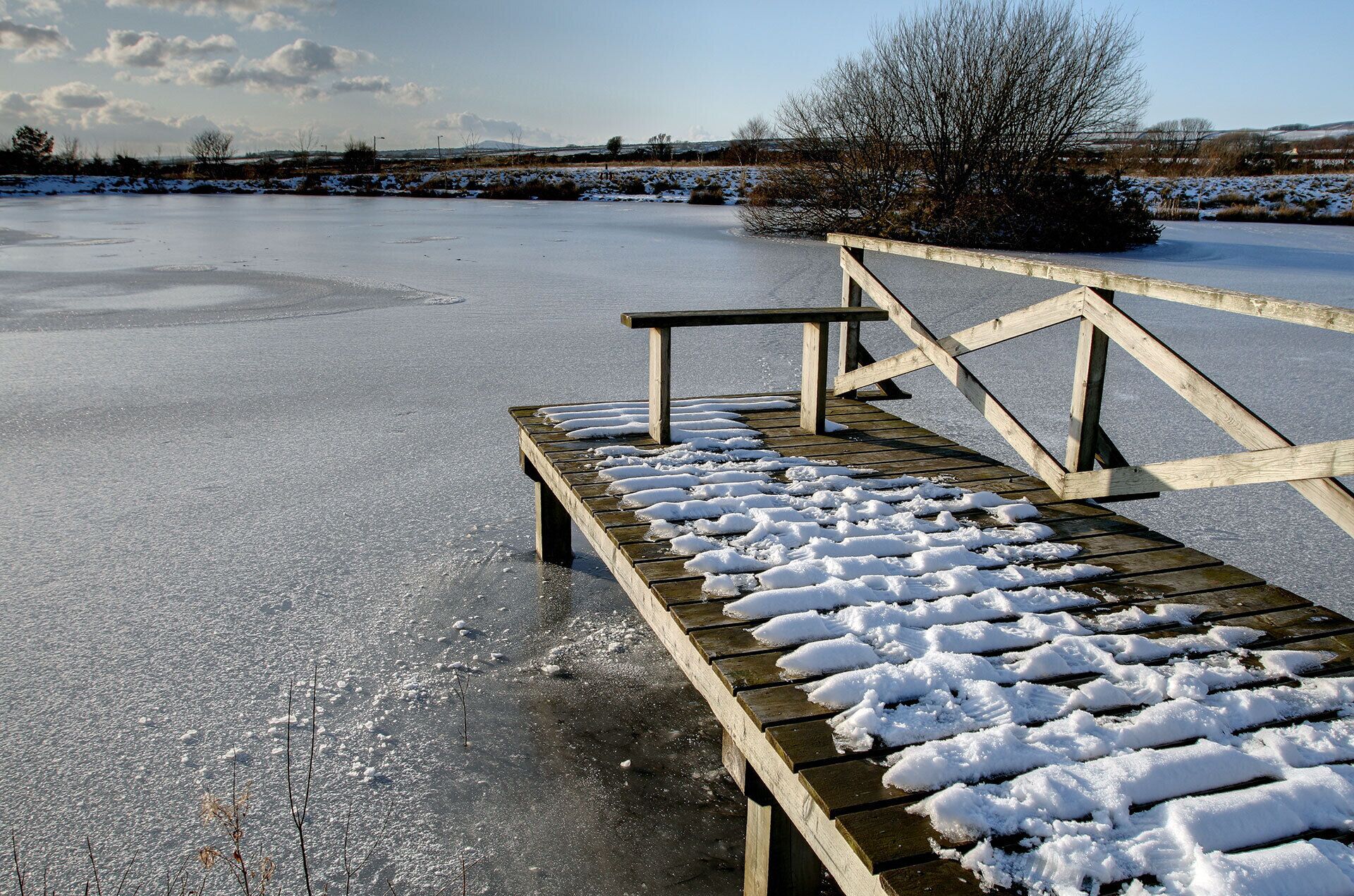 A wooden bench on a frozen lake with snow on the ground and a clear sky.