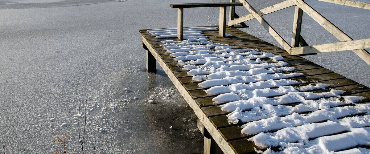 A wooden bench on a frozen lake with snow on the ground and a clear sky.
