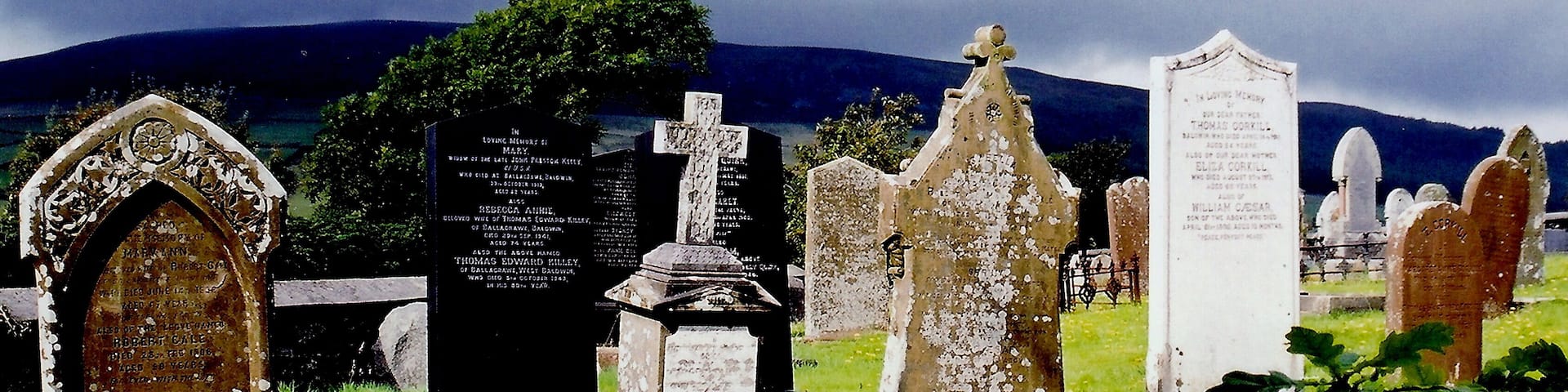 East Baldwin - St Luke's Church - Gravestones View is to the southwest from St Luke's Church graveyard towards B36. The lighting got my attention, as the gravestones were illuminated against the dark sky over the mountain in the background.