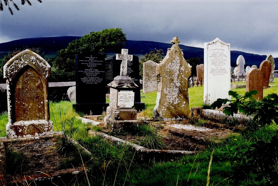 East Baldwin - St Luke's Church - Gravestones View is to the southwest from St Luke's Church graveyard towards B36. The lighting got my attention, as the gravestones were illuminated against the dark sky over the mountain in the background.