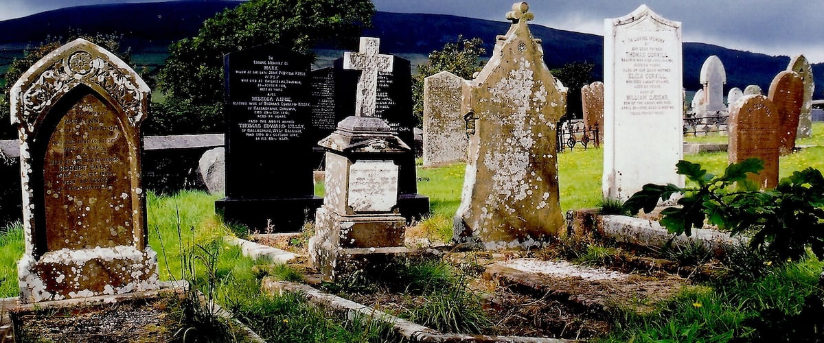 A cemetery with various gravestones and headstones, including a prominent cross and a memorial plaque.
