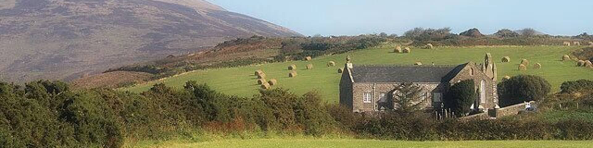 A rural landscape with a church, rolling hills, and scattered haystacks.