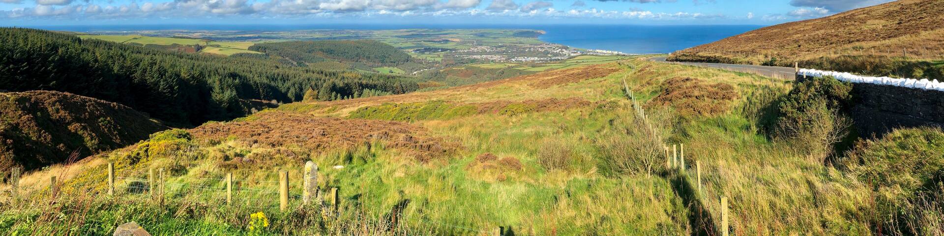 A coastal landscape with a road, rolling hills, and a distant view of the sea.