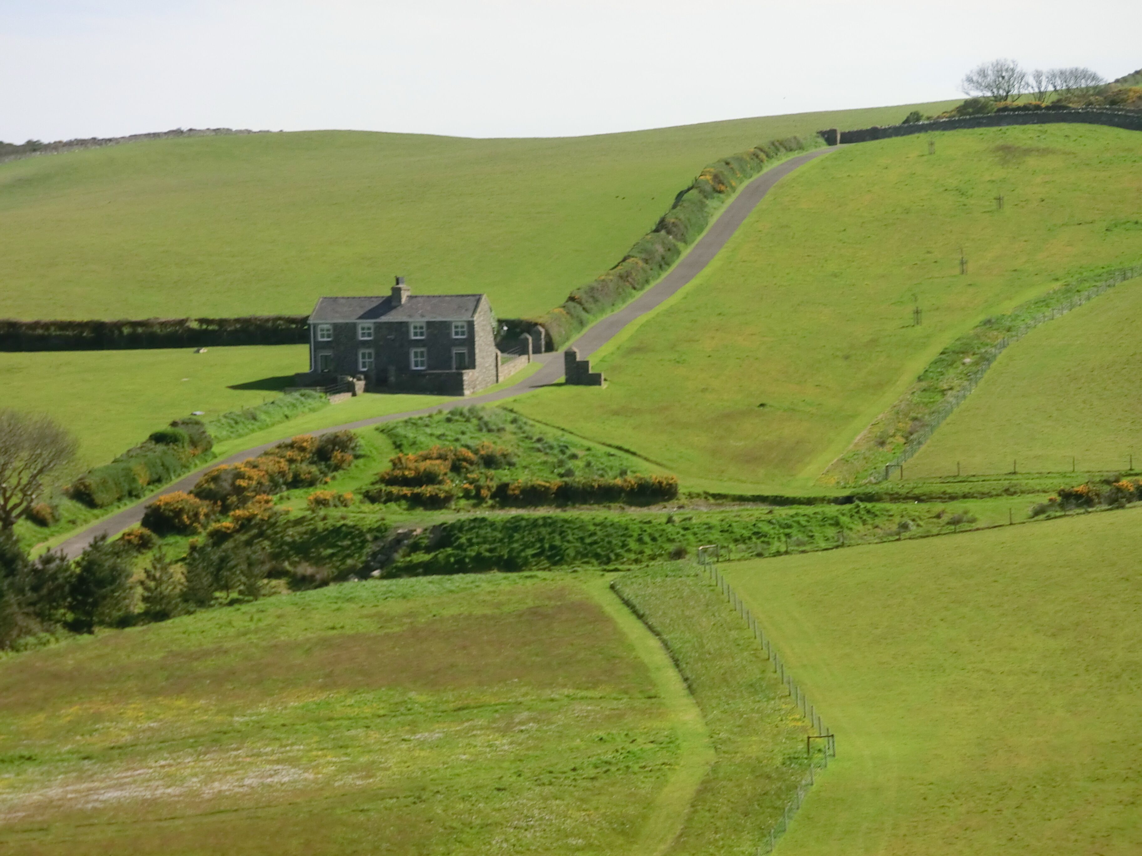 A stone house on a green hill with a winding road.