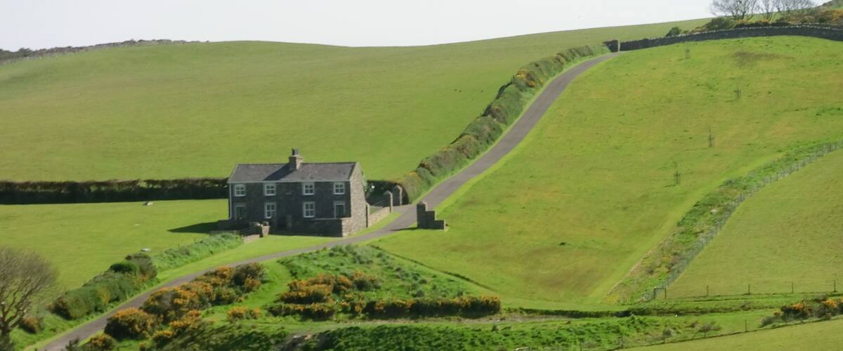 A stone house on a green hill with a winding road.
