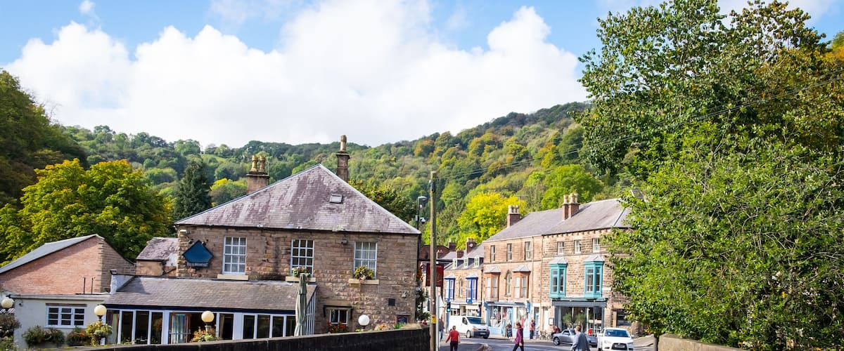 A street with historic buildings, a stone wall, and a hill in the background.
