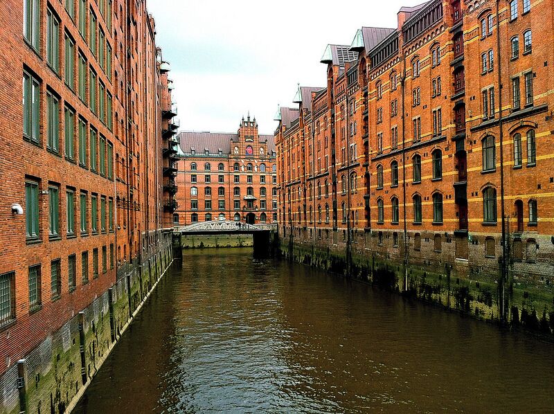 A canal flanked by historic brick buildings with a bridge in the background.
