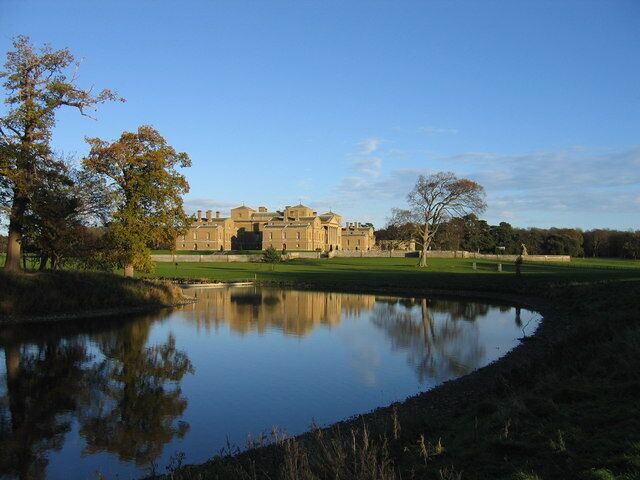 A large building with a pond in front, surrounded by trees and grass.