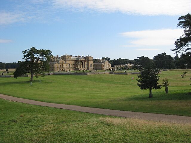 A large, historic building with a well-maintained lawn and a paved path in the foreground.