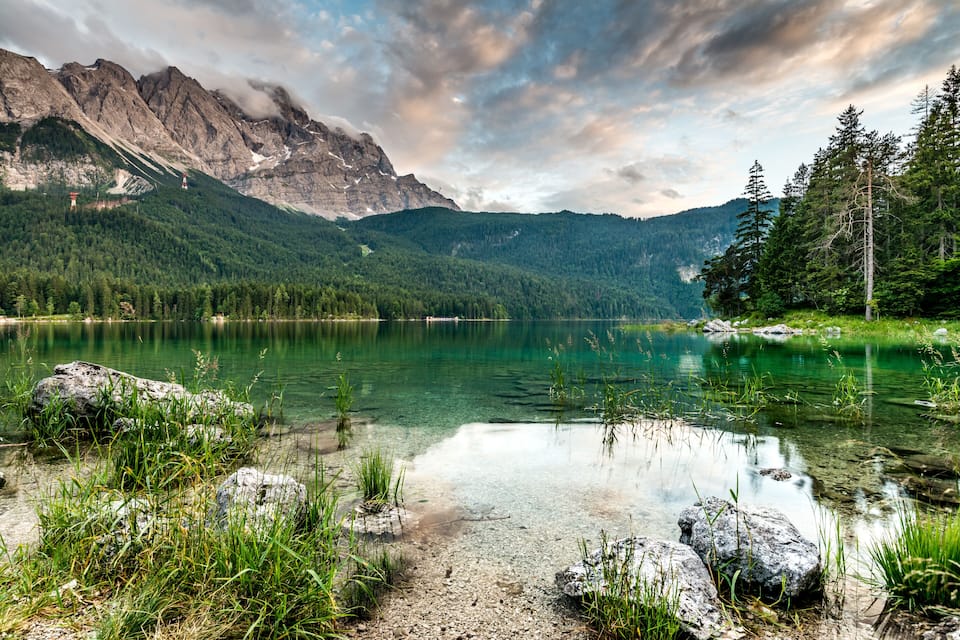 A mountain lake with clear water, surrounded by forest and rocky mountains.