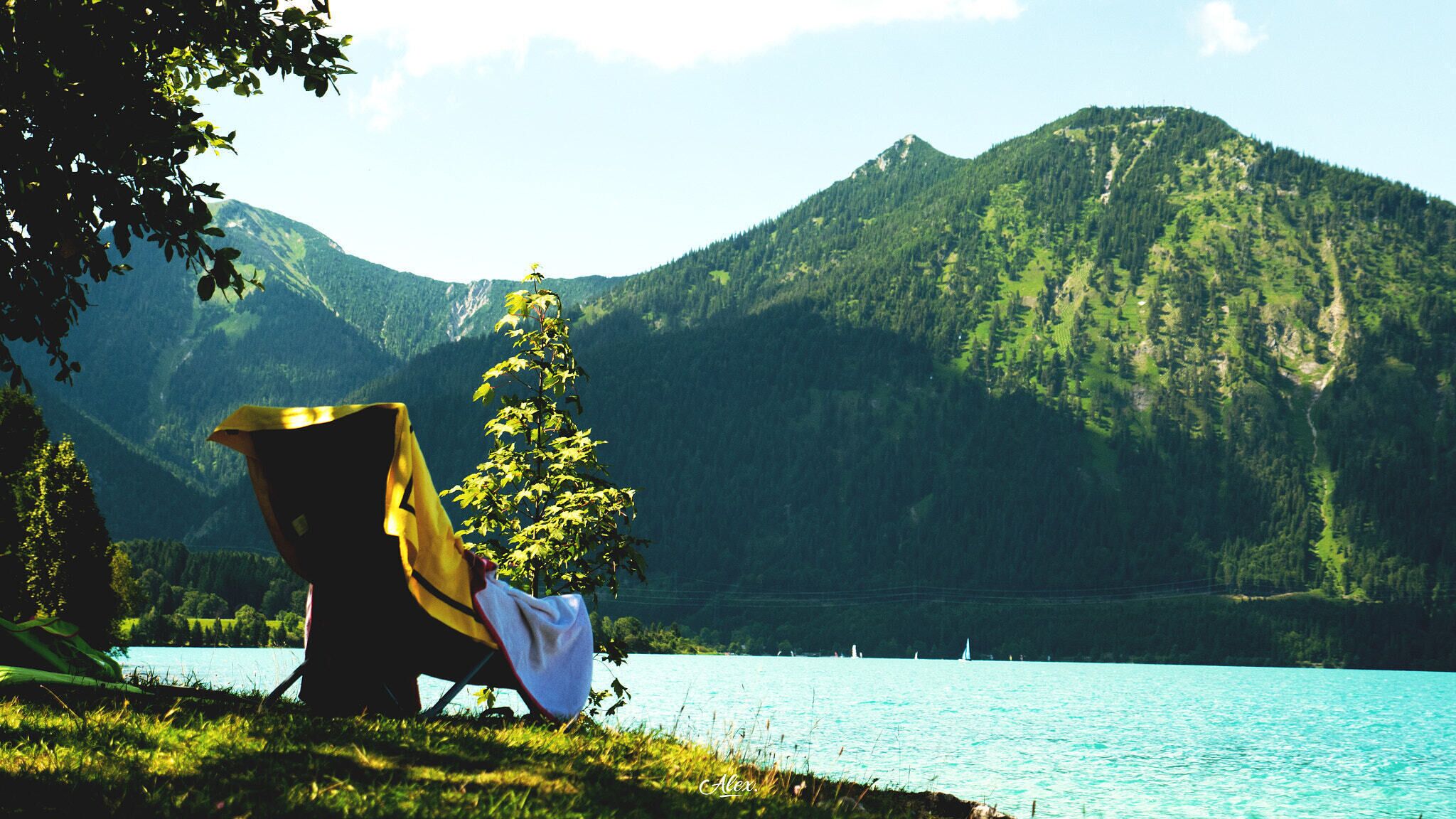 A chair by a lake with mountains in the background.