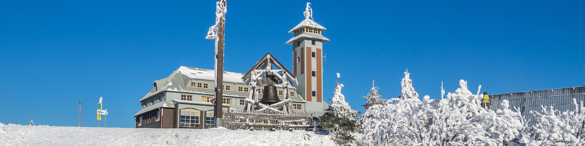 Ein mit Schnee bedecktes Gebäude mit einem Glockenturm und einer großen Glocke, umgeben von schneebedeckten Bäumen.