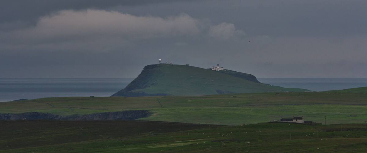 A coastal landscape with a prominent hill featuring a lighthouse and a radar station.