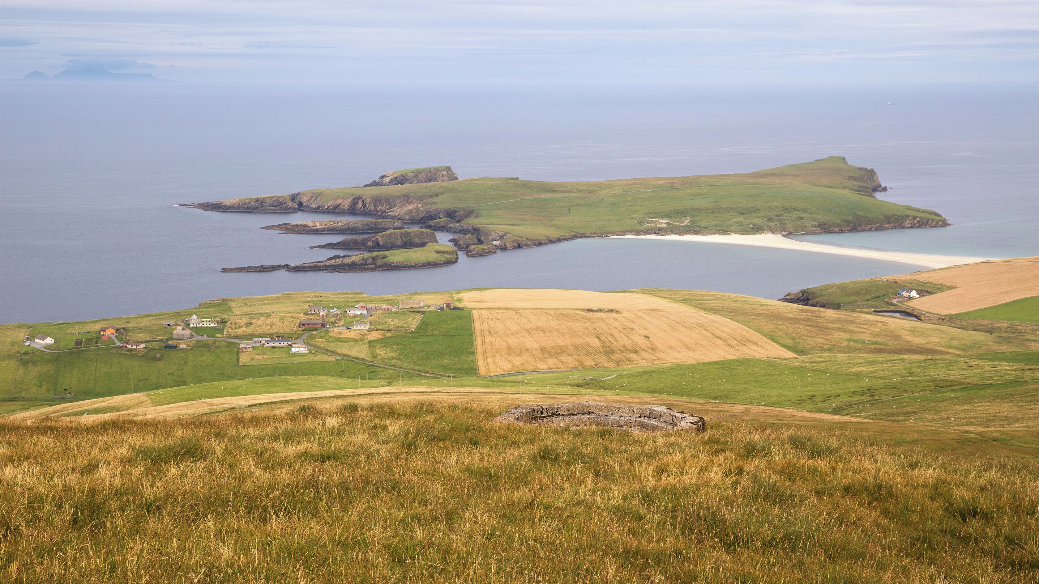 A coastal landscape with rolling hills, a small settlement, and a bay with a sandy beach.