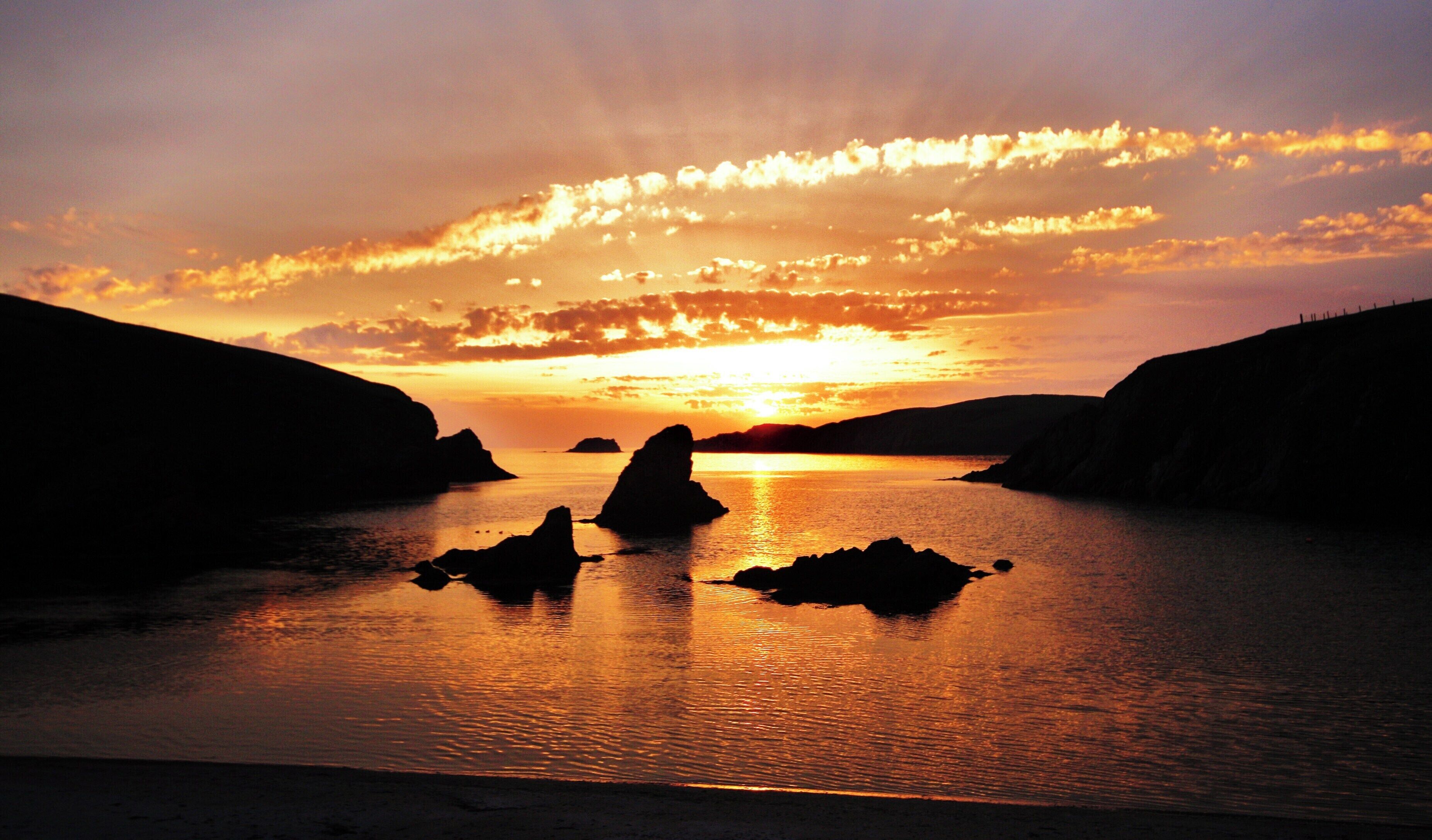 A sunset over a calm body of water with rock formations silhouetted against the sky.