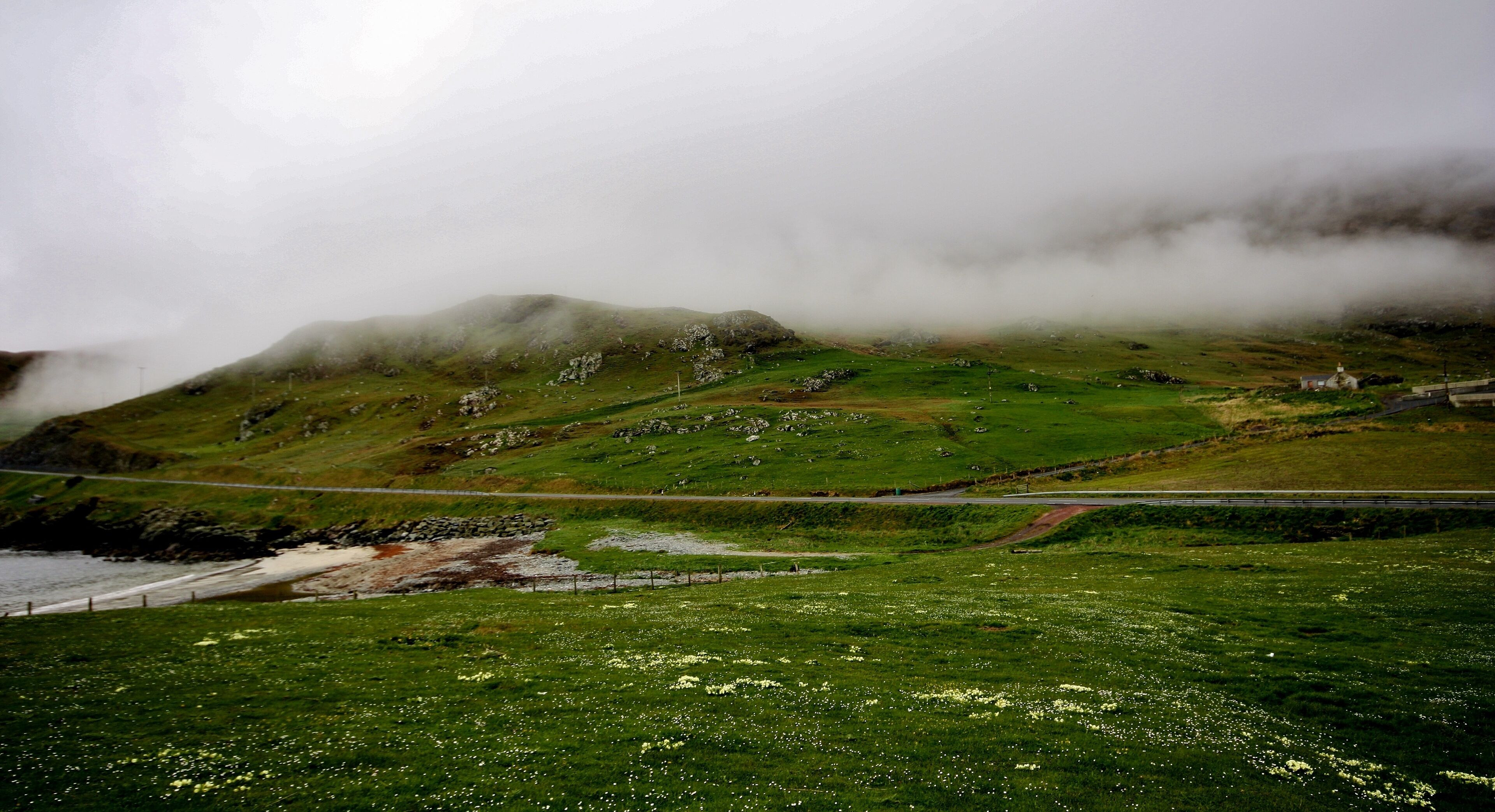A coastal landscape with green fields, a rocky hill, and a bridge.