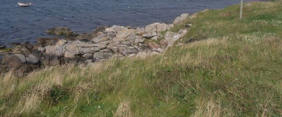 A rocky shoreline with a grassy foreground and calm sea.