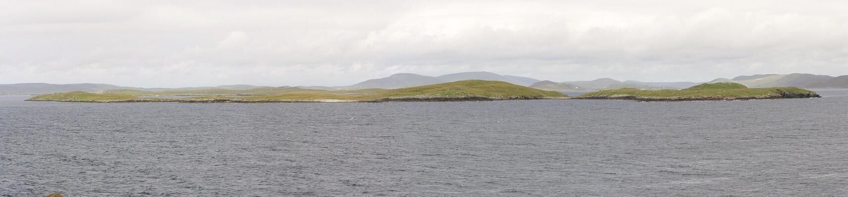 A calm sea with a small island covered in grass and surrounded by hills.