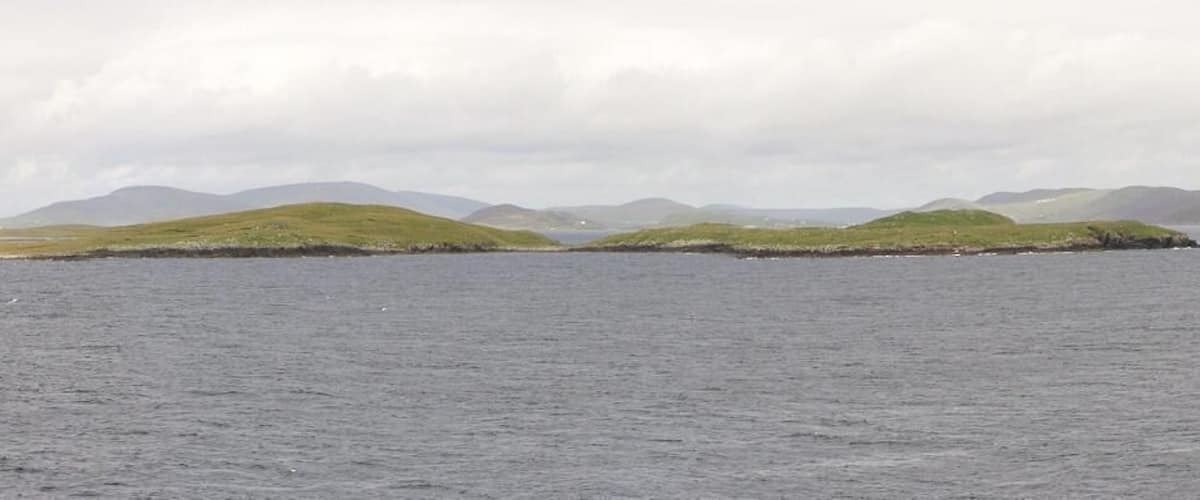 A calm sea with a small island covered in grass and surrounded by hills.