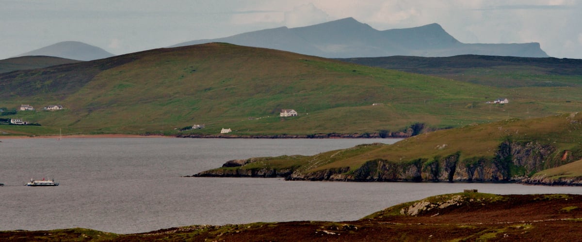 A coastal landscape with rolling hills, a body of water, and a distant mountain range.