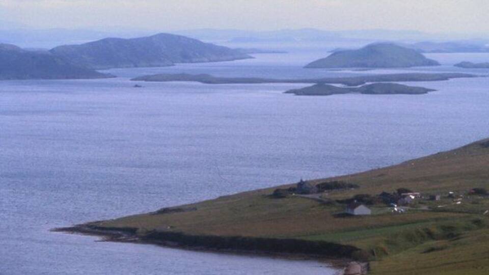 A coastal landscape with a small settlement by the water, surrounded by hills.