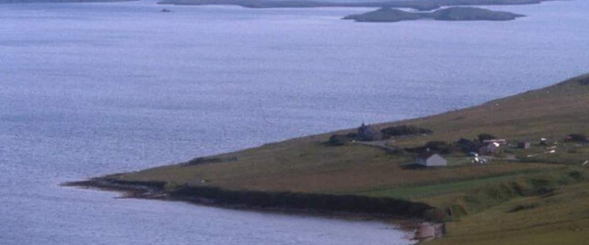 A coastal landscape with a small settlement by the water, surrounded by hills.