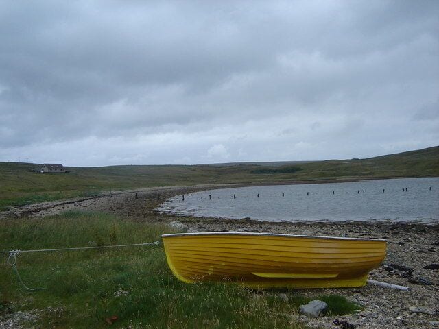 A yellow boat on a grassy shore near a body of water with a cloudy sky.