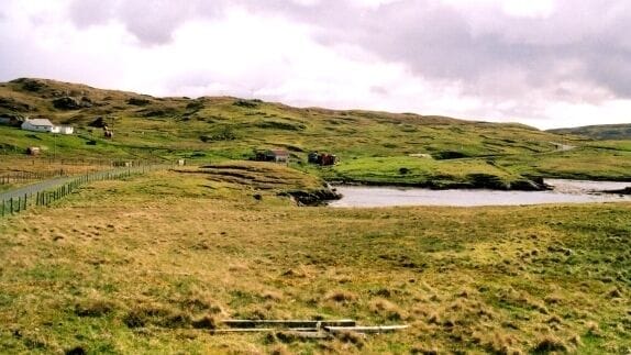 Paisaje rural con colinas ondulantes, un arroyo pequeño y una zona vallada.