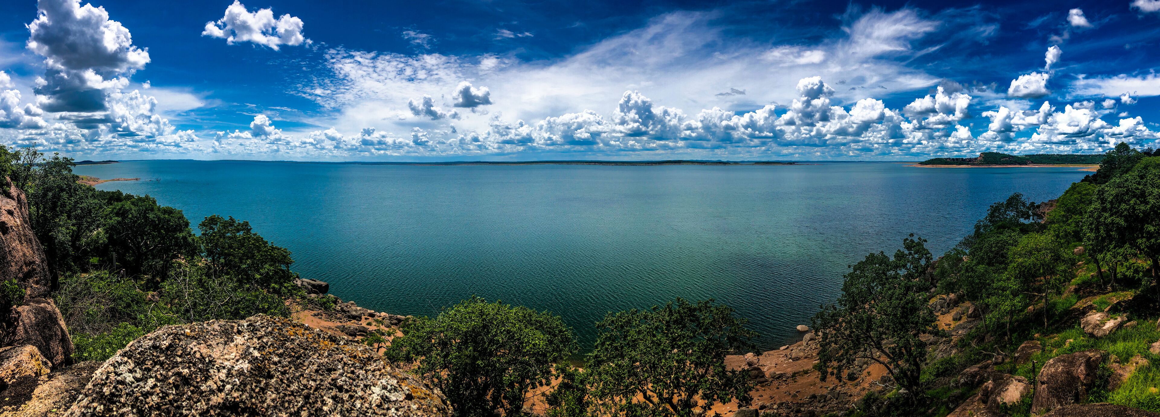 A coastal landscape with a calm sea, rocky cliffs, and dense greenery.