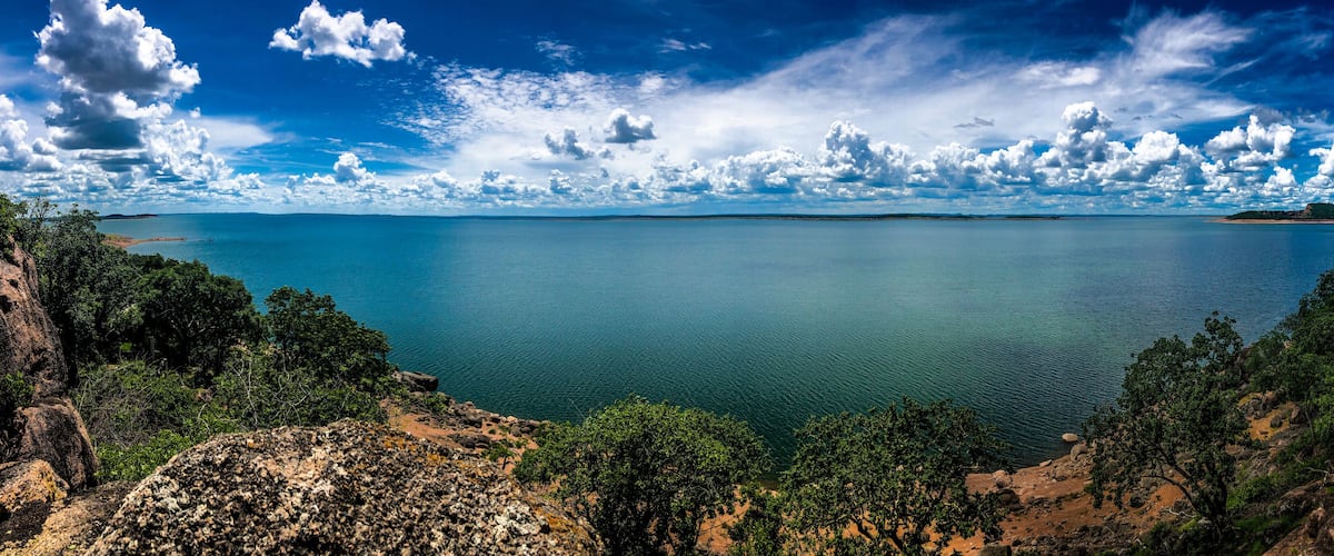 A coastal landscape with a calm sea, rocky cliffs, and dense greenery.