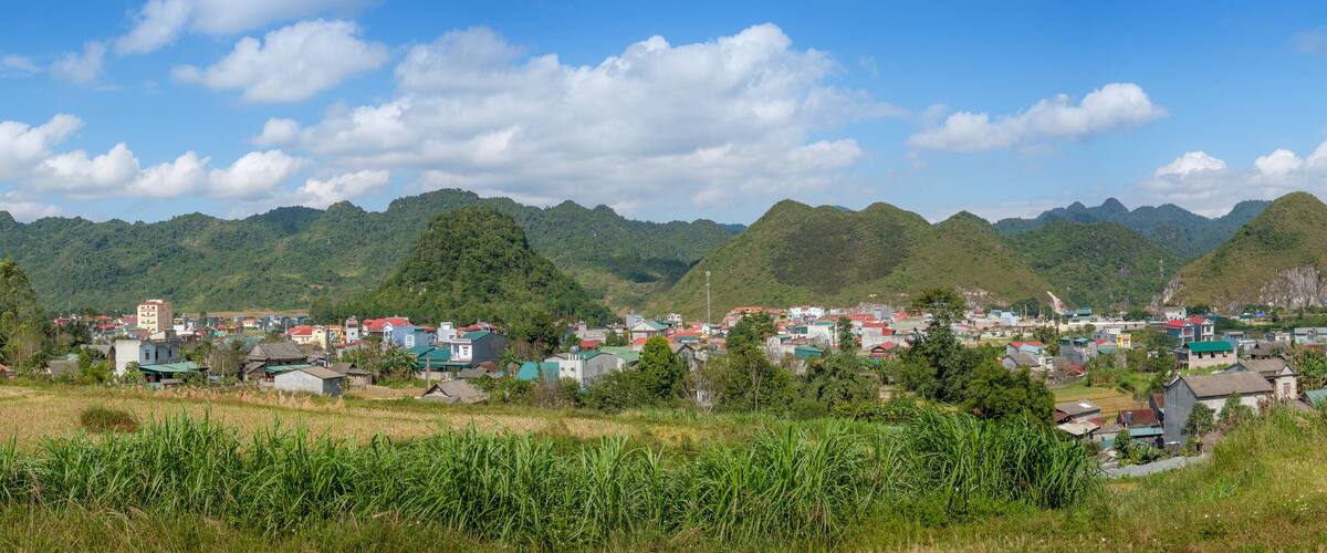 A village nestled in a valley with lush green hills and mountains in the background.