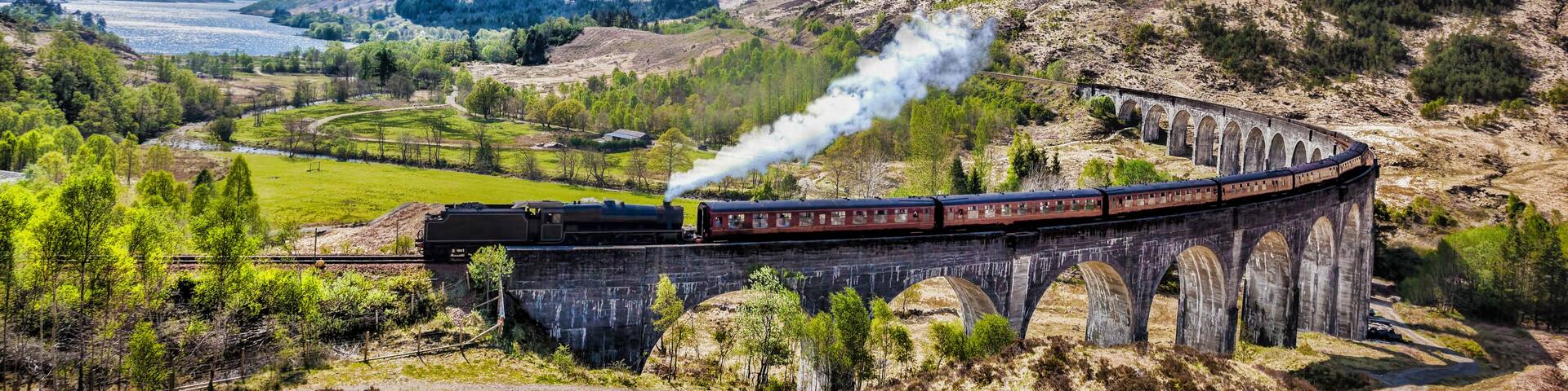Glenfinnan Railway Viaduct in Scotland with the Jacobite steam train against sunset over lake