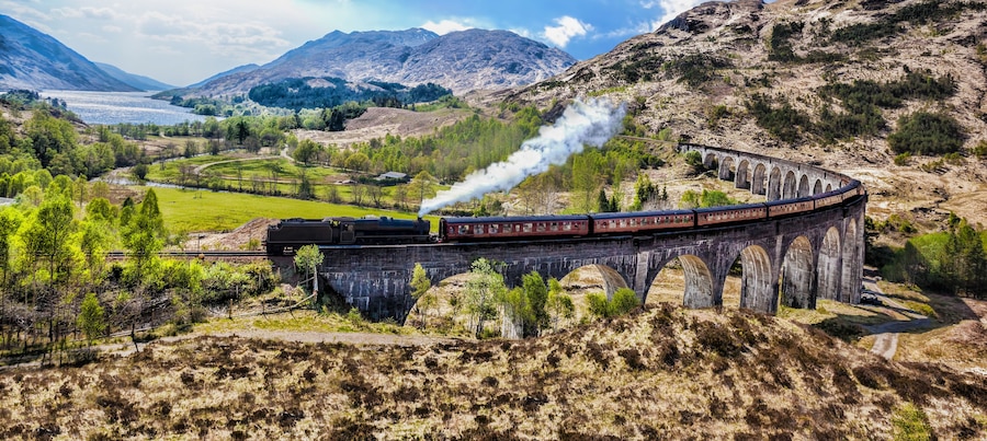 Glenfinnan Railway Viaduct in Scotland with the Jacobite steam train against sunset over lake