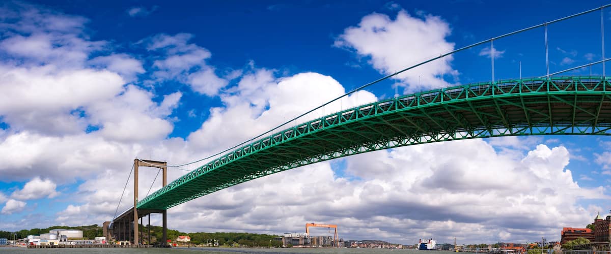 A green bridge spanning a body of water with a cityscape in the background.