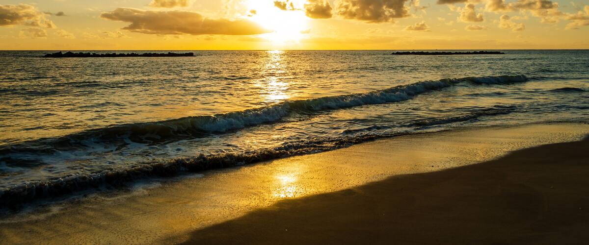 A sunset over a beach with waves and a distant pier.