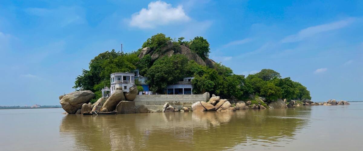 A rock formation with a small building on top, surrounded by water.
