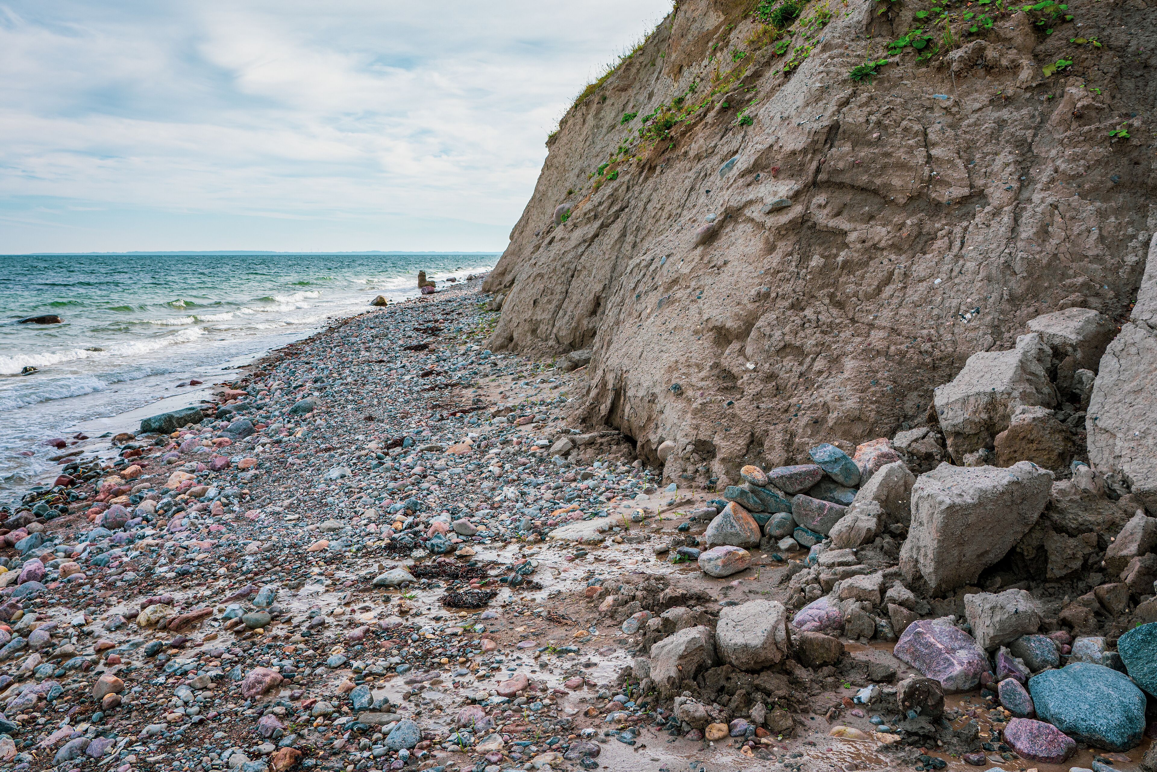 A rocky beach with a steep cliff and the ocean in the background.