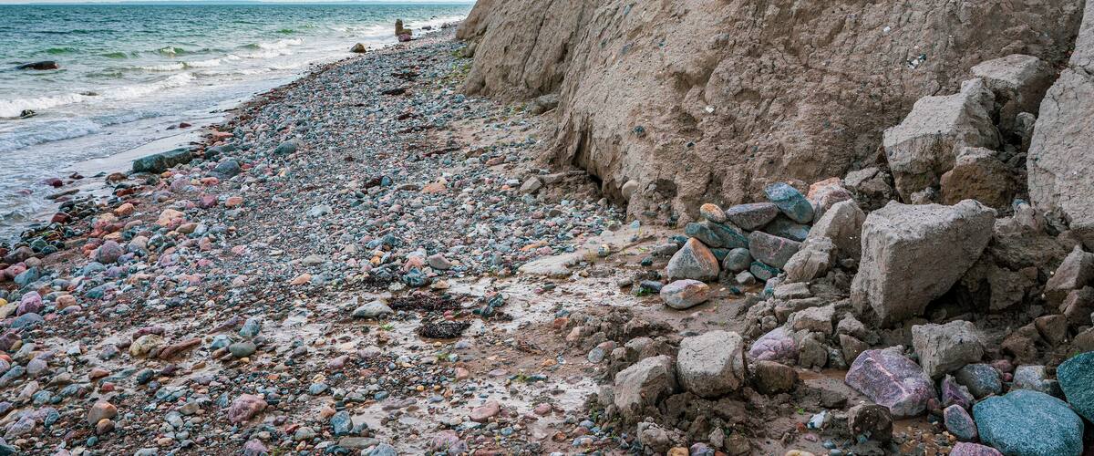 A rocky beach with a steep cliff and the ocean in the background.