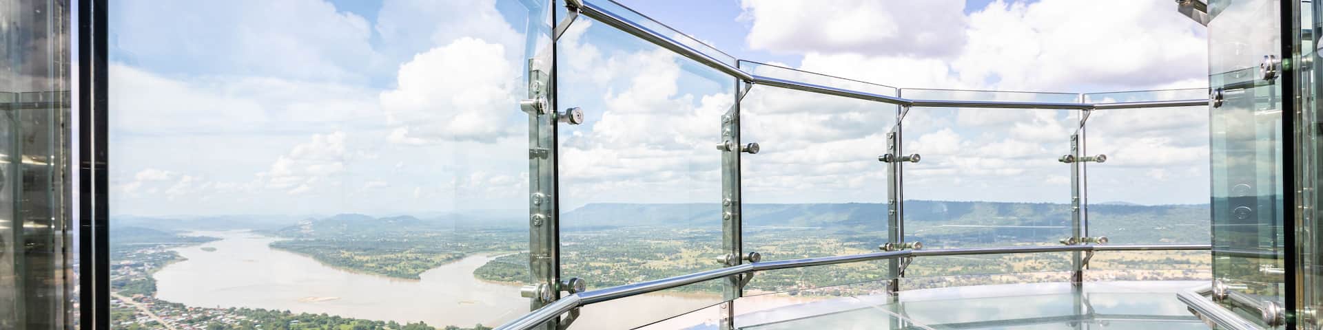 A glass observation deck with a metal railing overlooking a river and landscape.