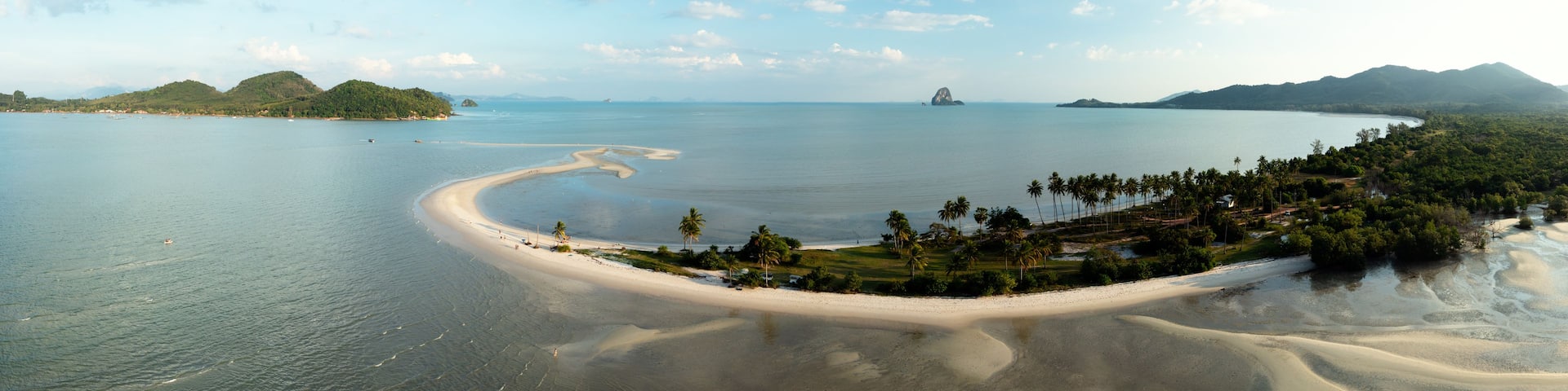 A coastal landscape with a sandy beach, palm trees, and distant mountains.