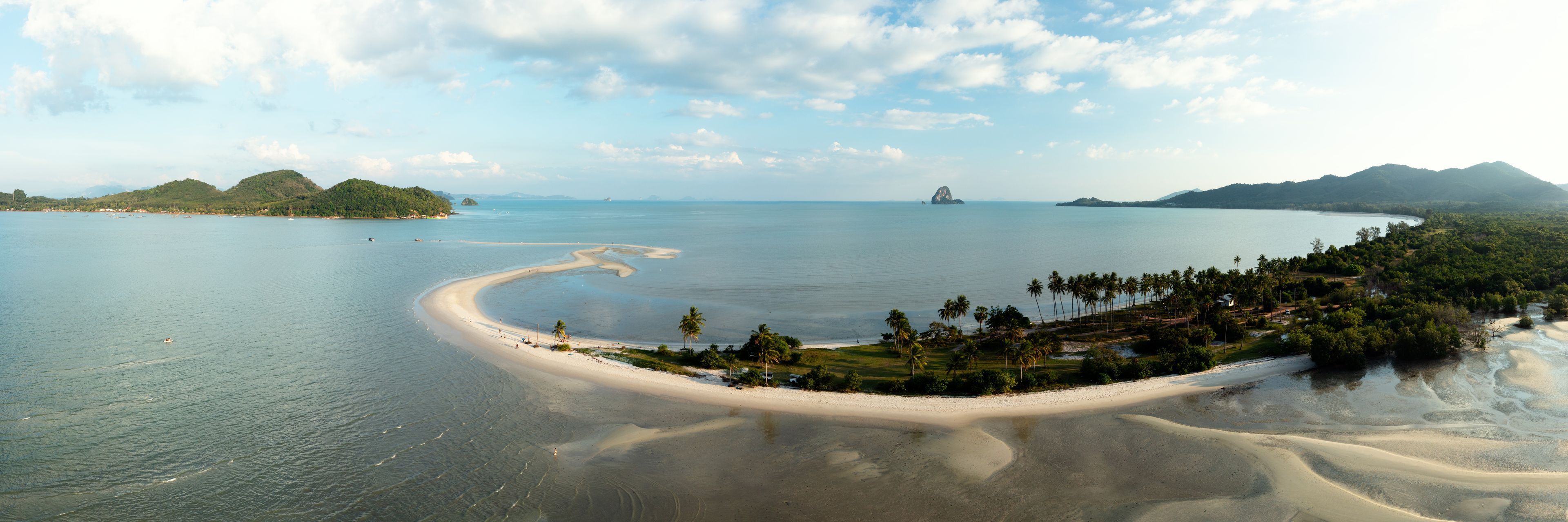 A coastal landscape with a sandy beach, palm trees, and distant mountains.