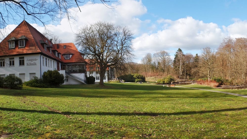 Ein Haus mit rotem Dach und weißen Wänden, umgeben von einem grasbewachsen Bereich und Bäumen.