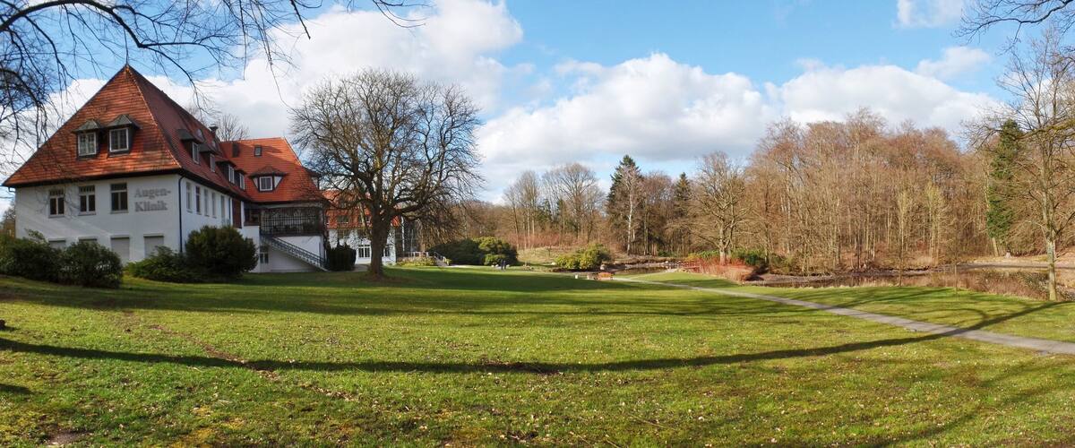 A house with a red roof and white walls, surrounded by a grassy area and trees.