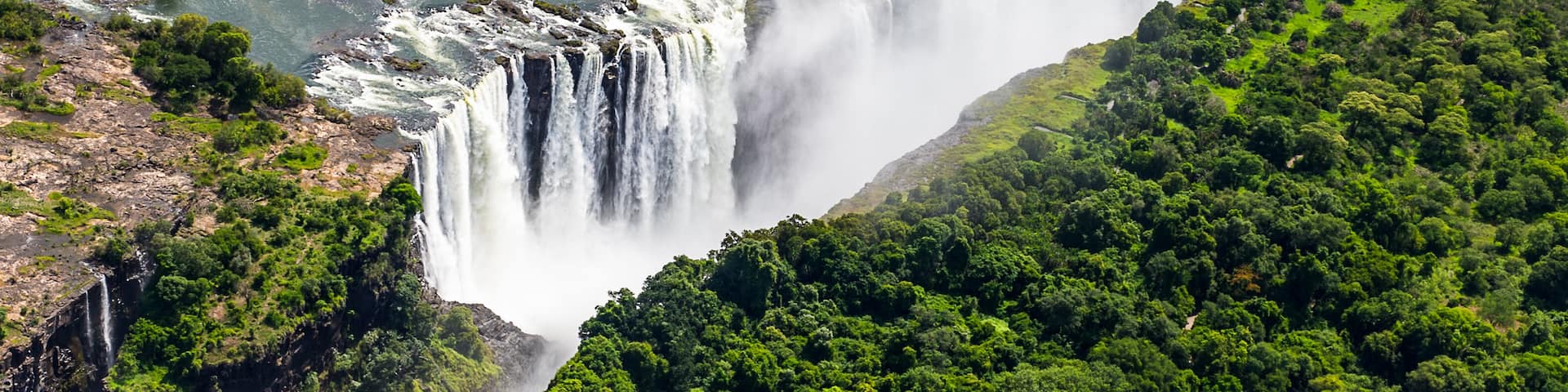 A large waterfall cascading down a steep cliff surrounded by lush greenery.