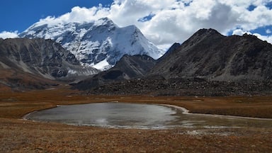 A snow-capped mountain, a clear blue sky, and a small lake surrounded by barren land.