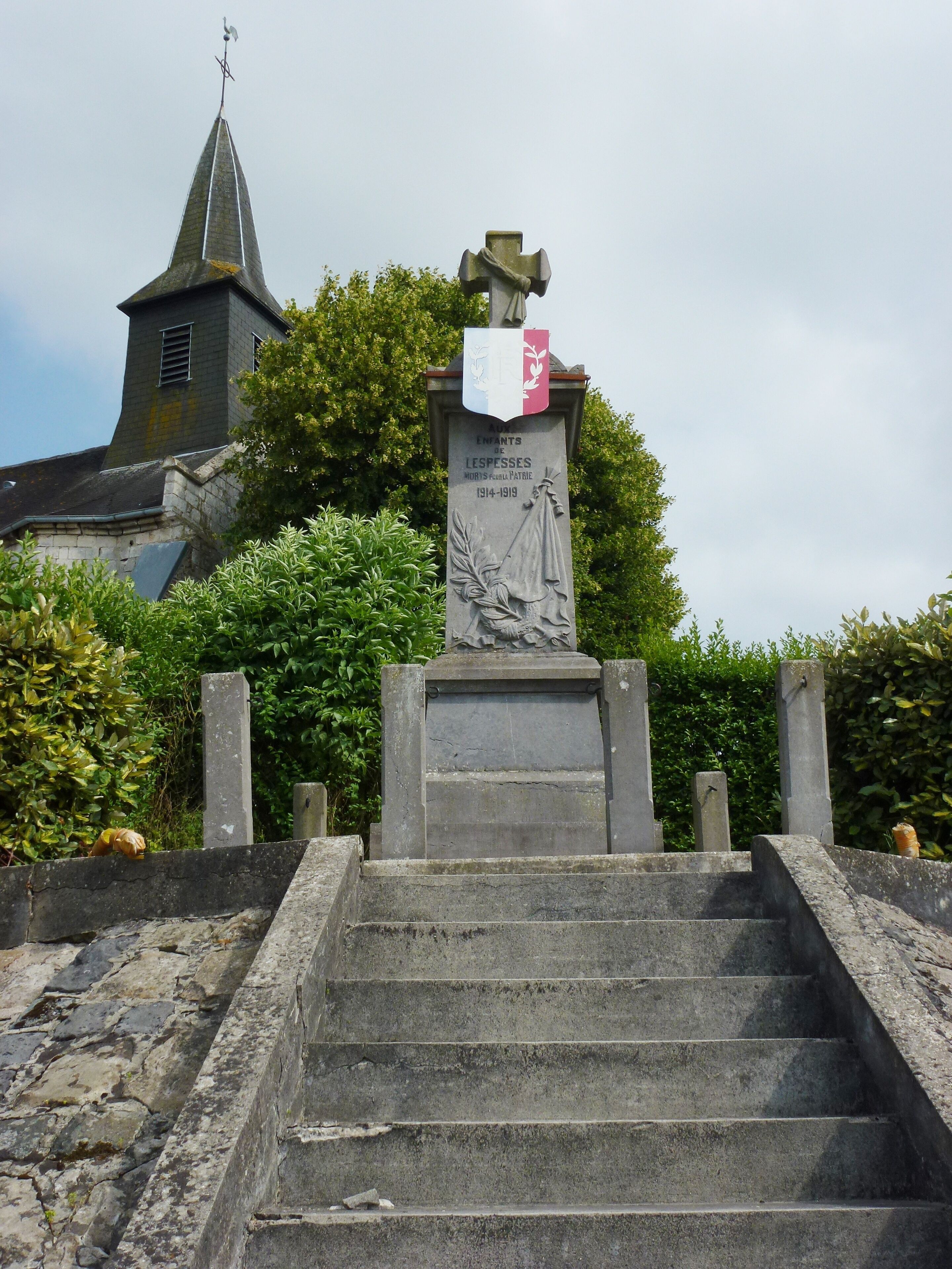 A stone monument with a cross and a plaque, surrounded by stone steps and greenery.