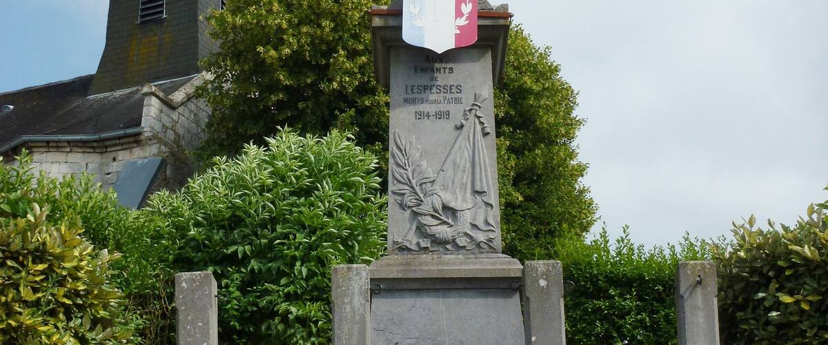 A stone monument with a cross and a plaque, surrounded by stone steps and greenery.