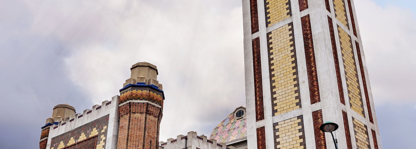 Um edifício histórico com uma torre de relógio, trabalhos em tijolo elaborados e uma estátua.