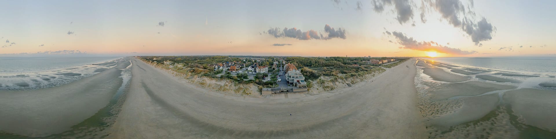 A coastal landscape with a beach, a town, and a sunset.