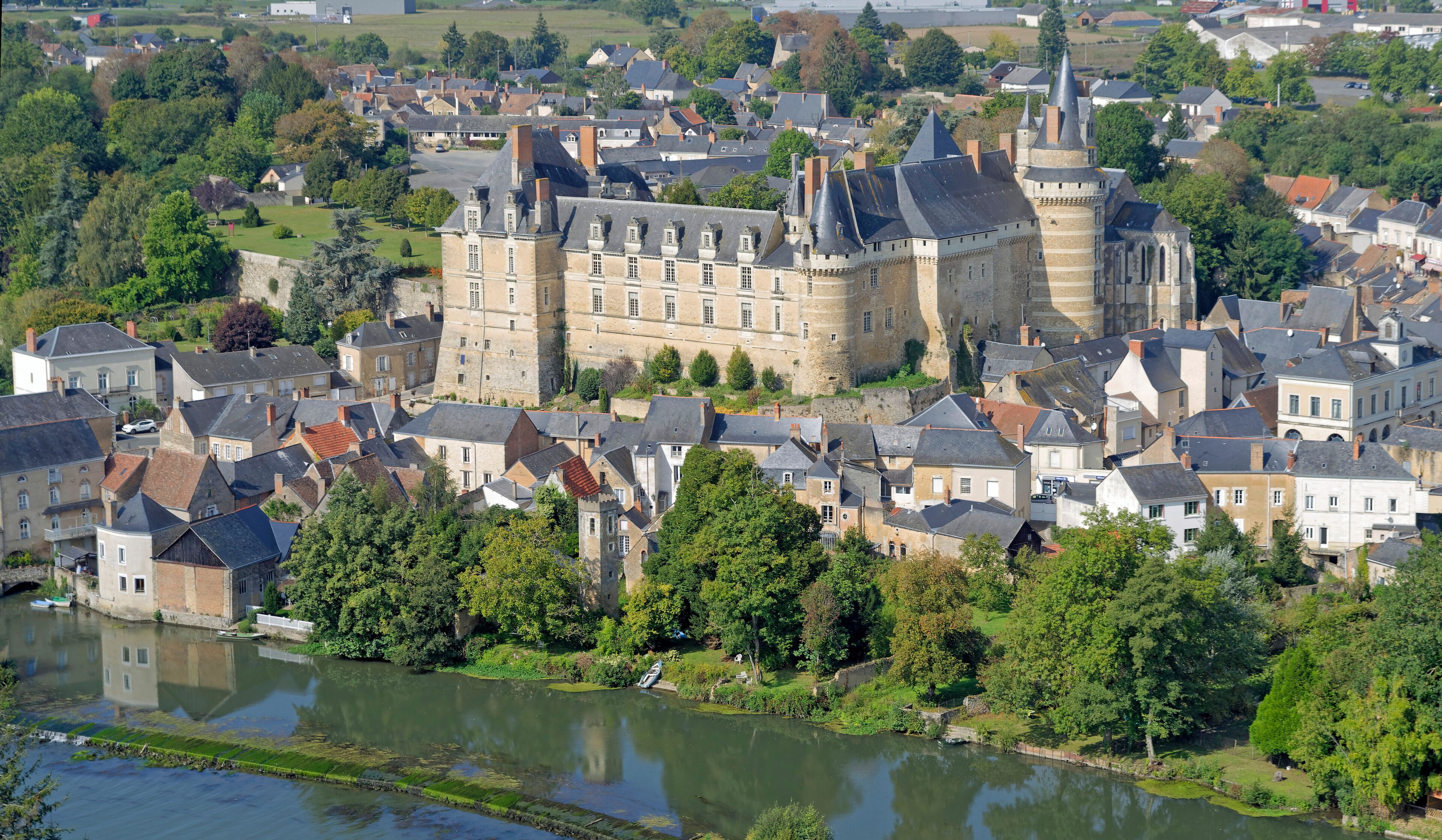 A historic town with a prominent castle, a river, and surrounding greenery.